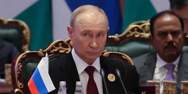 Володимир Путін сидить за столом на офіційній зустрічі з російським прапором