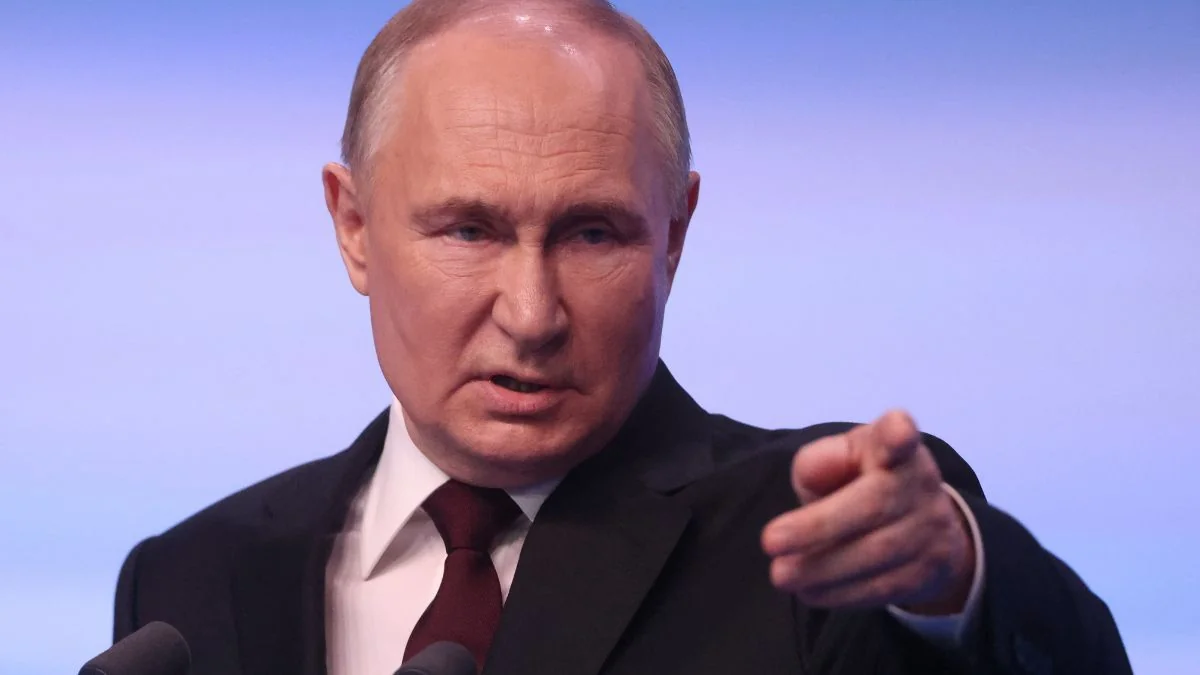Володимир Путін у темному костюмі вказує пальцем біля мікрофонів