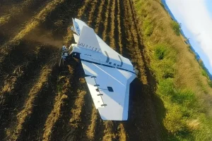 Білий безпілотник лежить на зораному полі серед борозен