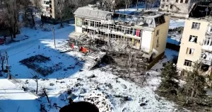 Зруйнована жовта будівля з проваленим дахом серед снігу та воронкою