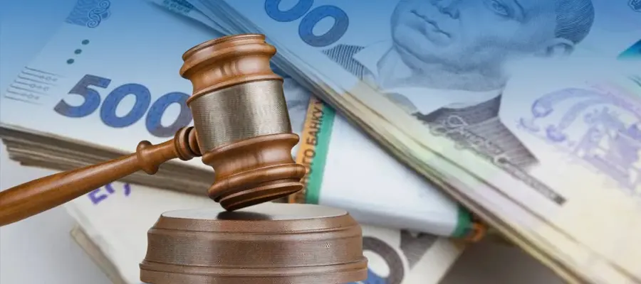 Дерев’яний судовий молоток на підставці на тлі купюр 500 гривень