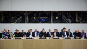Учасники засідання за столом із табличками країн і прапорами України