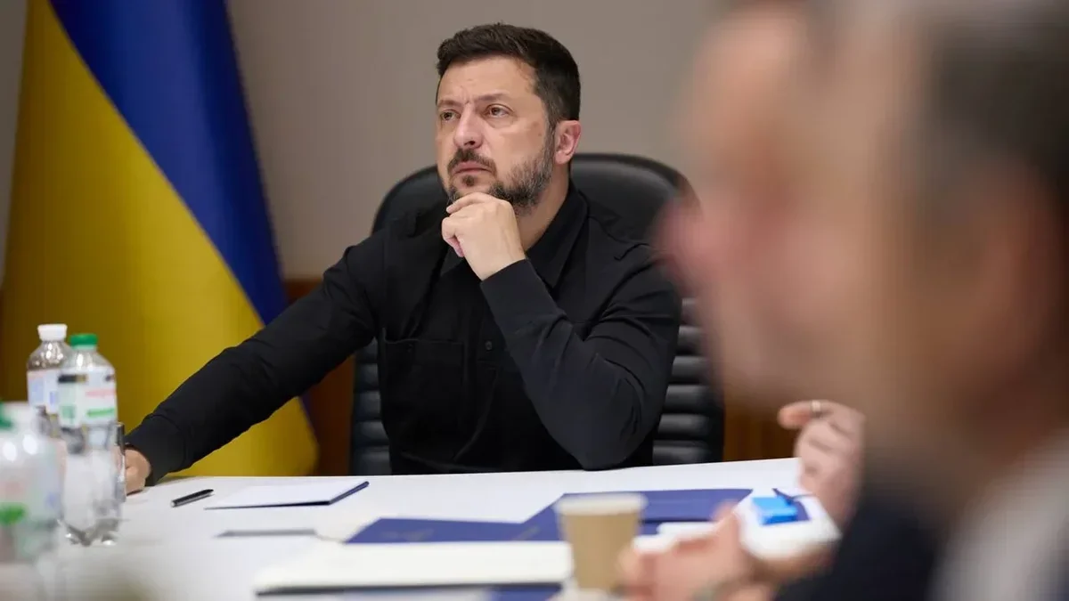 Зеленський у чорній сорочці сидить за столом на нараді біля українського прапора