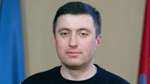 Чоловік середнього віку в чорній футболці на тлі синього та червоного прапорів