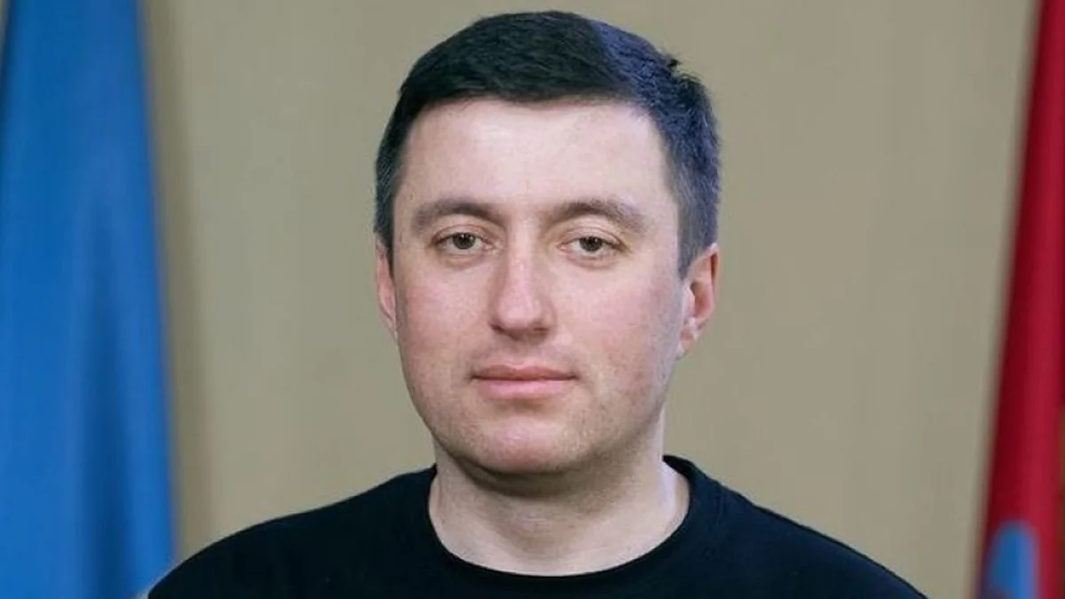 Чоловік середнього віку в чорній футболці на тлі синього та червоного прапорів